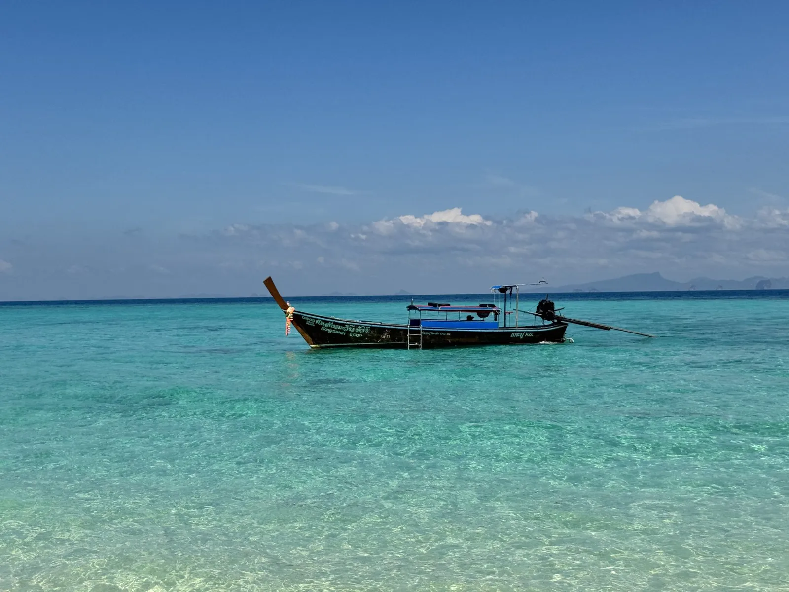 A wooden longtail boat floating on clear turquoise water off the Andaman coast