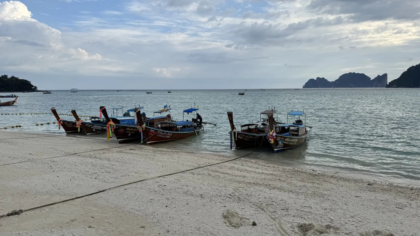 Longtail boats with garlanded bows lined up on a sandy beach